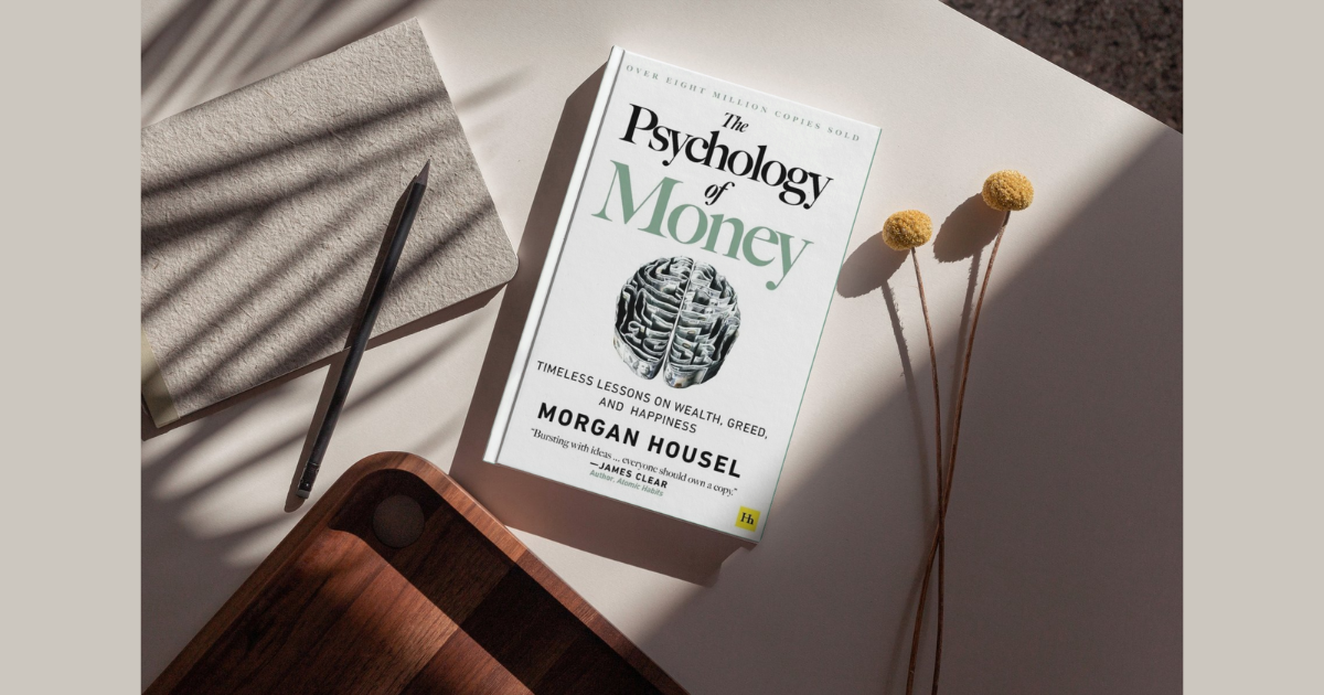 The Psychology of Money by Morgan Housel book with notebook, pencil, and dried flowers on a neutral desk